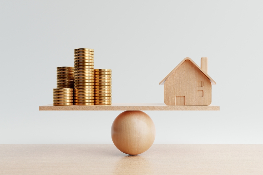wooden house and coins balancing on a scale