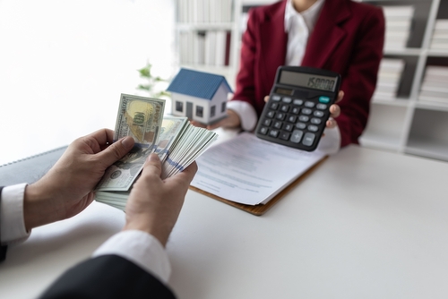 cash in hands being ready to be handed to someone who is holding a calculator and a model home